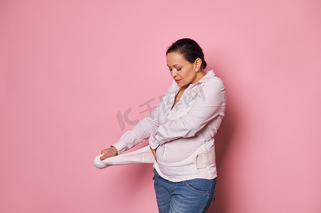 孕妇穿上支撑绷带以减轻背痛，孤立的粉红色。