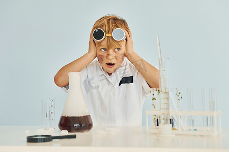 扮演了摄影照片_穿着外套的害怕的小男孩用设备在实验室里扮演科学家