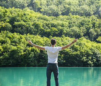 年轻人张开双臂在湖前享受自由