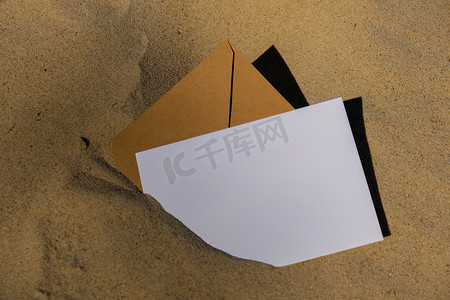 米色自然色调的信封，上面有空白的白纸便条复制空间，供您在沙滩上的文字中使用。
