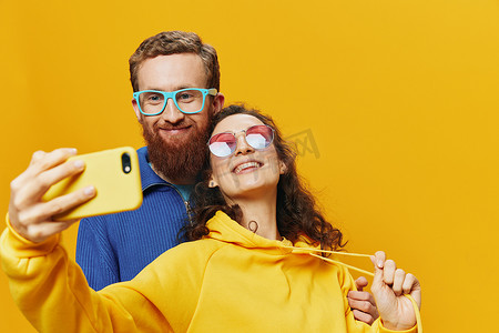 在黄色背景下，女人和男人带着手机的搞笑情侣手握社交网络和歪歪扭扭的交流自拍微笑很有趣。
