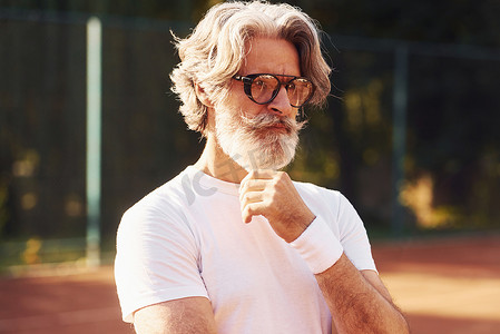 网球场上戴眼镜、白衬衫和黑色运动短裤的高级时尚男士