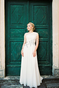 一件白色礼服的新娘靠着一扇绿色的门站立