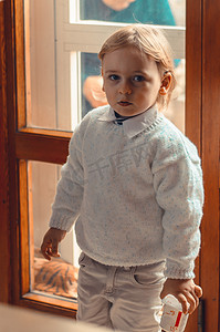 帅气的金发小男孩站在窗边，手里拿着酸奶