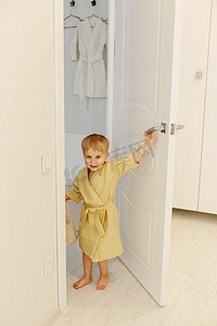 一个穿着黄色浴袍的男孩站在浴室的入口处，微笑着