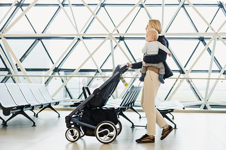 母亲带着他的婴儿男婴，在机场出发航站楼推着婴儿车前往登机口登机。