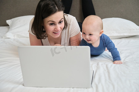 有婴儿躺在家里床上的女人饶有兴趣地看着笔记本电脑