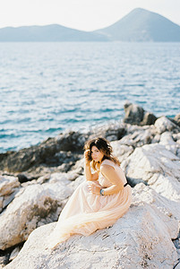 新娘坐在海边的岩石上，用手托着头