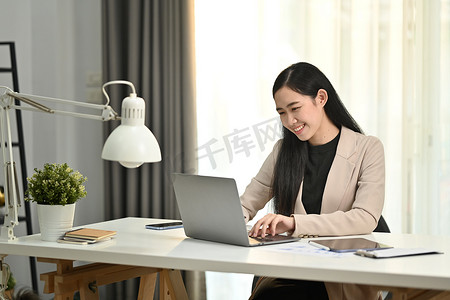 穿着时尚西装、面带微笑的年轻女性专属经理在笔记本电脑显示器上查看商务电子邮件