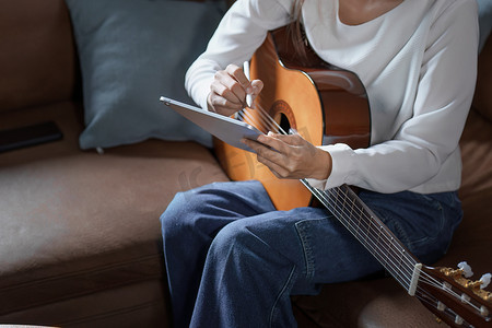 亚洲年轻女性在沙发上弹吉他放松度假压力的画像