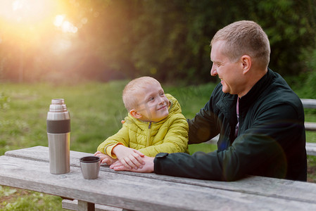 幸福的家庭：父亲和孩子男孩儿子在秋天的公园里玩耍和大笑，坐在木凳和桌子上。