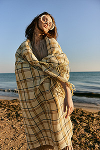日落时分，一个可爱的女人穿着格子呢站在沙滩上，风吹动着她的红头发。