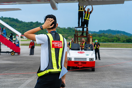 一名航空电子技术人员困惑地看着机场技术人员团队在出发前对客机的襟翼进行故障排除和维修。