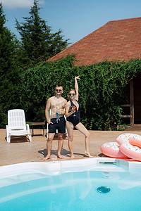 泳衣男人摄影照片_穿着泳衣的男人和女孩在蓝色泳池附近放松