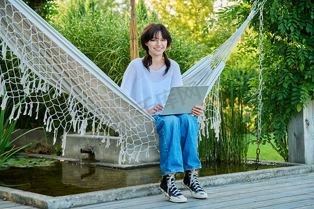 在吊床上放松的少女使用笔记本电脑进行休闲学习