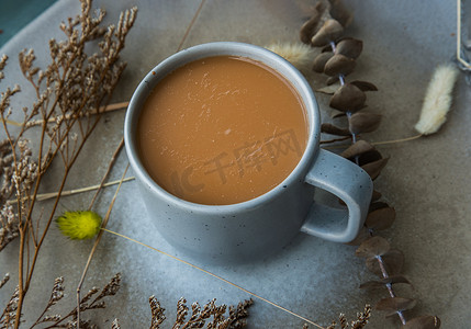 花背景奶茶摄影照片_蓝色陶瓷杯中的热橙奶茶、陶瓷上的甜茶泰式奶茶和陶瓷盘上的干花。