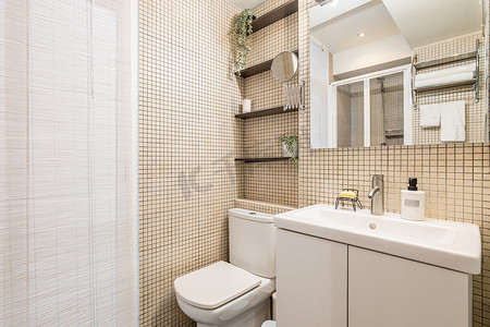 现代风格的浴室配有米色马赛克瓷砖、白色水槽和卫生间以及自然采光的大窗户。