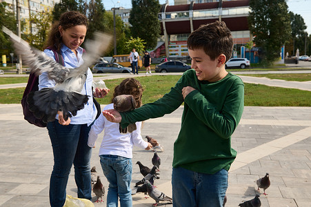 幸福的多民族家庭，慈爱的母亲和两个孩子在城市公园的广场上喂鸽子