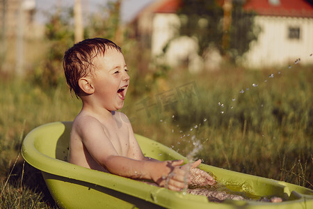 小男生在洗澡摄影照片_可爱的小男孩在花园里的户外浴缸里洗澡。