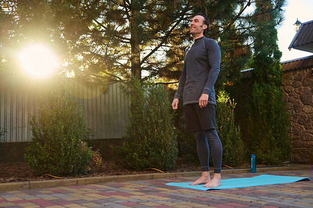 全长活跃男子、瑜伽运动员赤脚站在蓝色健身垫上，日落时在户外练习瑜伽