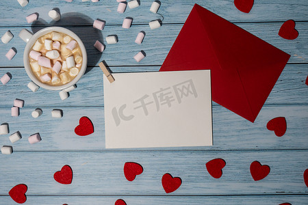 贺卡或邀请卡模拟与红色信封与白杯咖啡和棉花糖在木制背景。