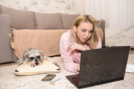 年轻女子正在笔记本电脑上工作，一只灰色的狗躺在她旁边的地毯上。