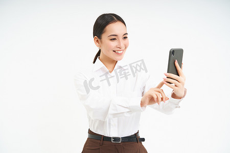 销售额摄影照片_美丽的微笑女商人在手机上自拍，在智能手机上拍照，录制视频，站在白色背景上