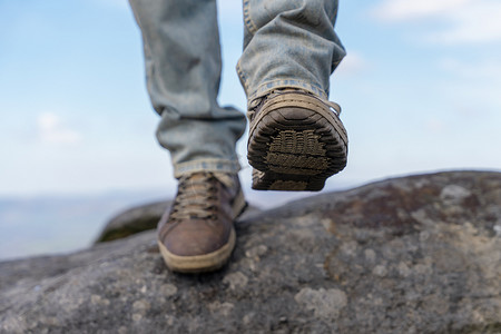 阳光明媚的日子里，身穿特殊靴子的男子在山上行走，到达目的地，在峰区的山顶上，在蓝色多云的天空下行走 旅行生活方式概念