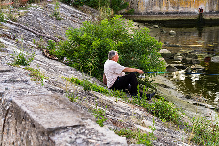 钓鱼竿钓鱼船摄影照片_男子在 Rom 的 Orsova 的河边放松和钓鱼