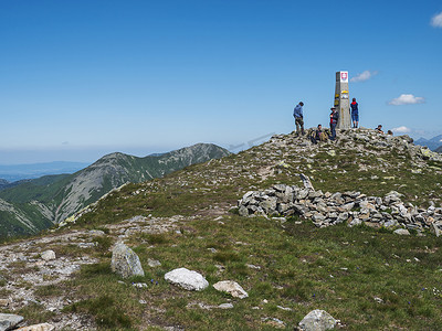 纹身图摄影照片_斯洛伐克，西塔特拉山，2019 年 7 月 4 日：一群徒步旅行者在西塔特拉山的 Baranec 峰顶休息，并欣赏 Rohace 全景。