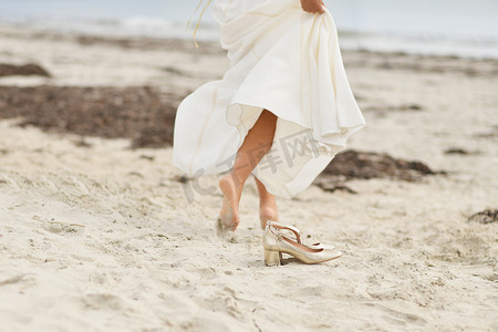 钻石海岸摄影照片_海滩上穿着白色礼服和金色鞋子的新娘