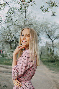 春天在樱花盛开的花园里散步的金发女孩。