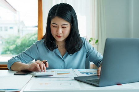 财务、规划、营销和会计，亚洲员工在工作中使用文档和计算器以及计算机检查财务报表的肖像