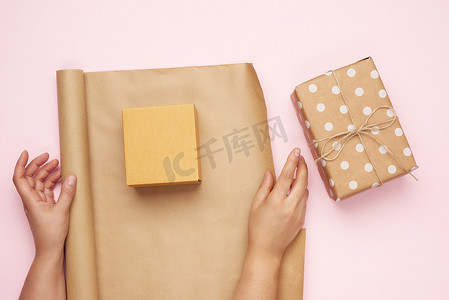 两只女手用棕色牛皮纸包装礼物，粉红色背景