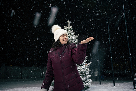 在下雪的夜晚，快乐的女人在城市街道上行走时，手上抓着雪花。