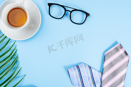 父亲节快乐背景概念，蓝色和粉色领带、眼镜、报纸、叶子和蓝色背景的茶杯，带有文本复制空间。