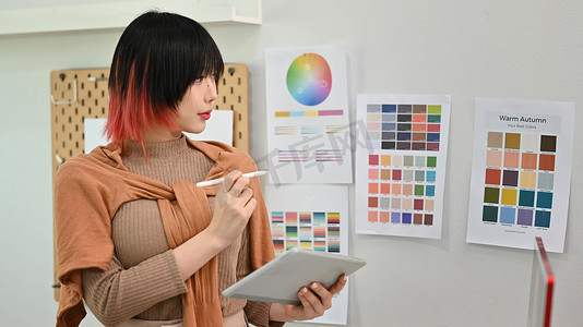 年轻的亚洲女设计师插画家站在现代设计工作室并使用数字平板电脑