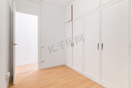 带白色镶板的内置宽敞衣柜和通往另一间铺有强化木地板的房间的门。