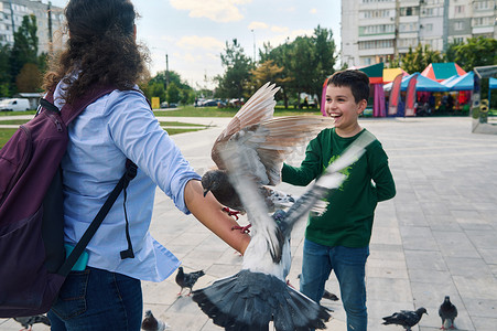 一个快乐的少年男孩在公园里与妈妈散步和喂鸽子时微笑着玩得开心的生活方式肖像