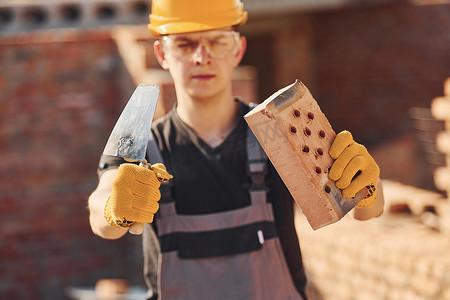 建筑工人穿着制服和安全设备站在建筑物上拿着砖块和工具的画像