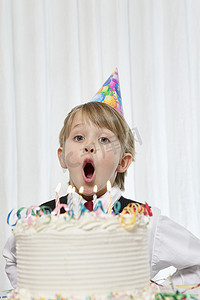 小男孩戴着派对帽在生日蛋糕上吹蜡烛的肖像