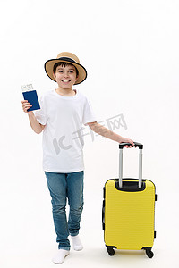 穿着休闲 T 恤、牛仔裤和草帽的十几岁男孩旅行者带着登机牌和白色背景的手提箱走路。
