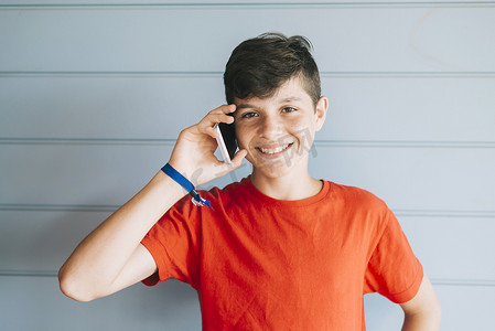 身穿红色 T 恤的年轻少年在使用电话时靠墙站立