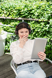 电脑聊天摄影照片_坦率地描绘一位年轻女子在户外戴着耳机通过平板电脑聊天