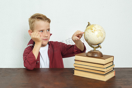 小学生坐在桌旁，用手撑着头，指着地球仪。