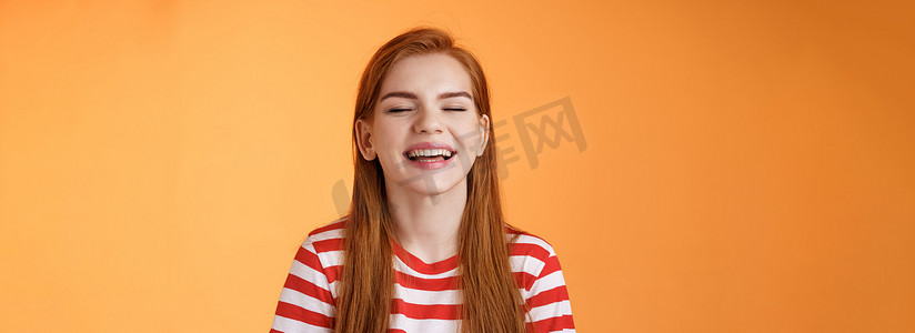 真诚倡议摄影照片_真诚快乐、魅力四射的红发女孩微笑着，闭上眼睛享受温暖的夏日阳光，欢快地笑着，感到放松的喜悦，露出洁白的牙齿，美好的假期概念，橙色背景
