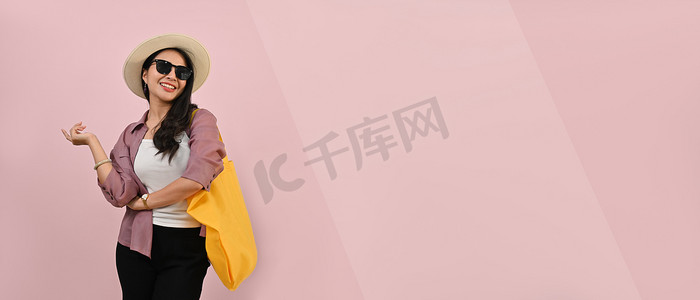 自信的女人穿着夏装、帽子和太阳镜，在粉红色背景中突显出来，并有平面设计的复制空间