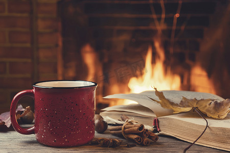 冬天的书摄影照片_红杯配热茶，壁炉前放着一本打开的书，壁炉概念的舒适、放松和温暖