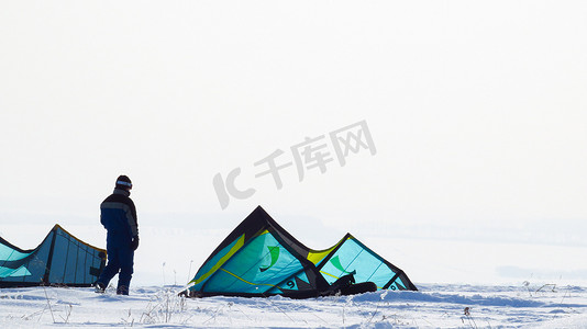 在多雪的冬季地形中，一个男人背对着绿色帐篷站立