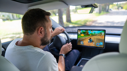 特斯拉的电动汽车摄影照片_俄罗斯新西伯利亚 — 10.08.2022：白人男子在驾驶特斯拉汽车时玩游戏。